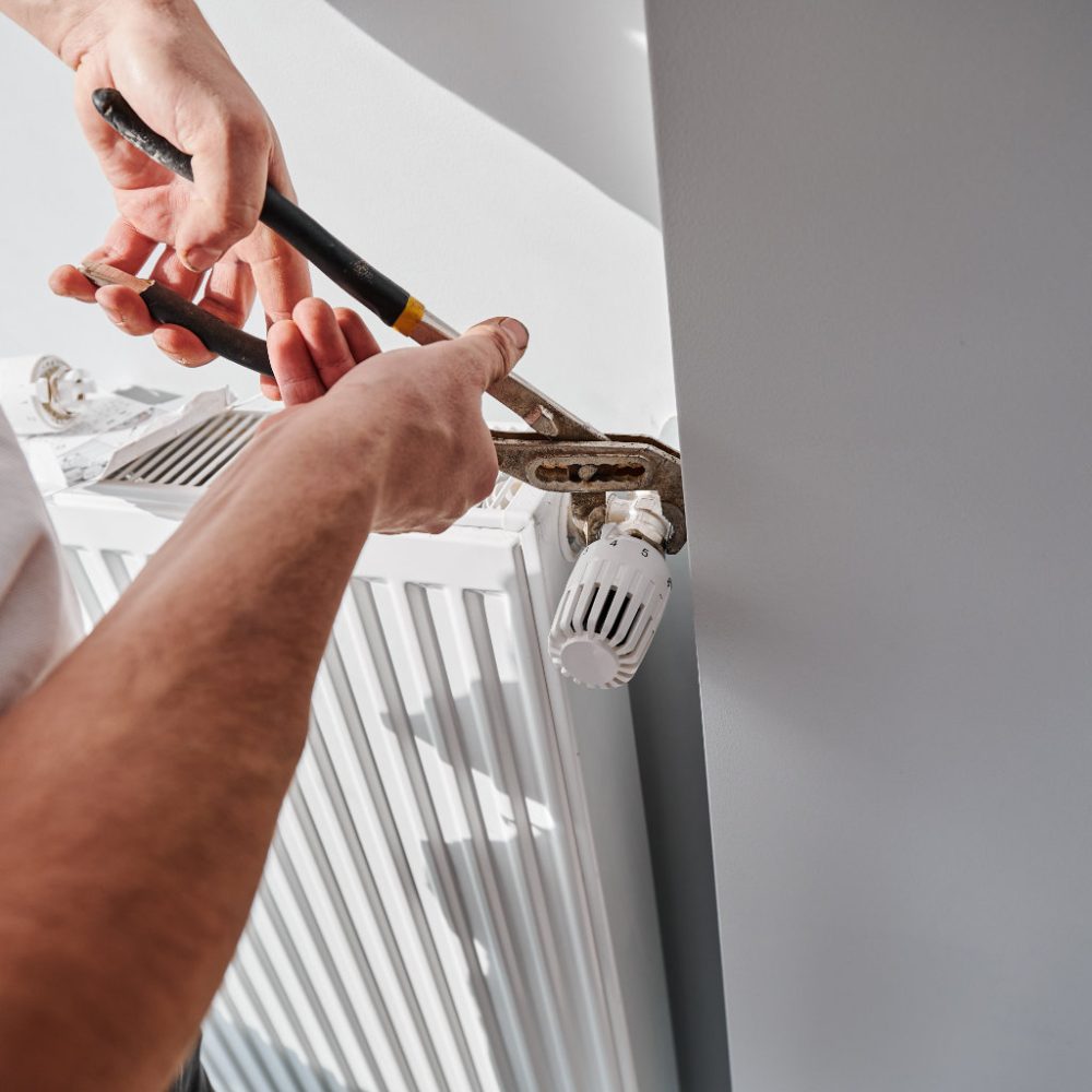 Close up of man using wrench tool while installing heating radiator in apartment under renovation. Male plumber working on heating system installation. Home renovation and plumbing works concept.